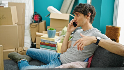Obraz premium Young hispanic man talking on smartphone sitting on sofa at new home