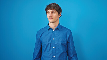 Young hispanic man looking to the side with serious expression over isolated blue background