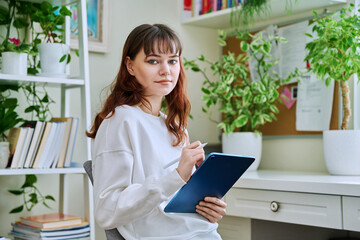 Young female teenager with digital tablet, stylus drawing illustrating sitting at home