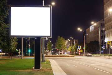 Large horizontal billboard in the night city. Bright lights of lanterns on poles near the road....
