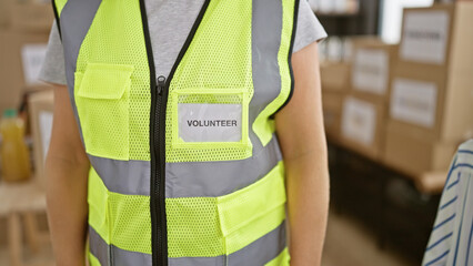 Beautiful blonde young woman volunteer, standing in reflective vest, serving in community charity center with altruism and unity