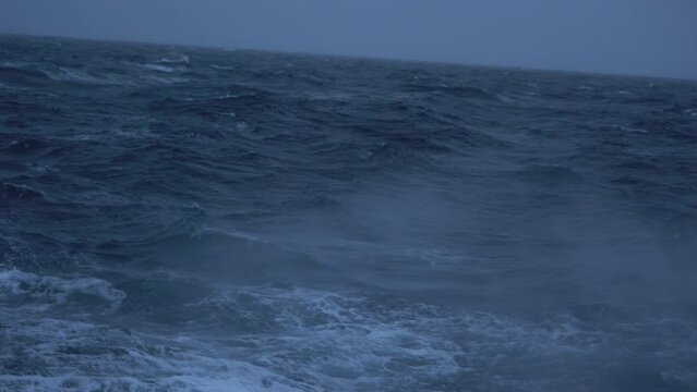 Storm. Sea. Splashes of waves fly by. View to waves low on water. Wind breaks waves with splashes. White foam on wind. Side view along ship.