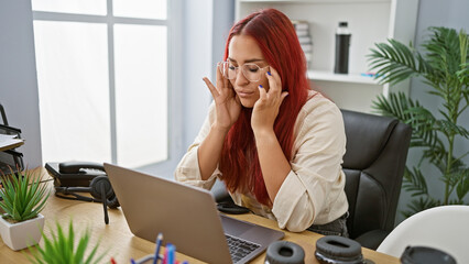 Stressed redhead young woman, an overworked business worker battling headache in office's hustle