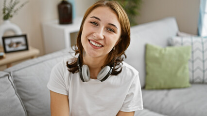 Young woman wearing headphones sitting on sofa smiling at home