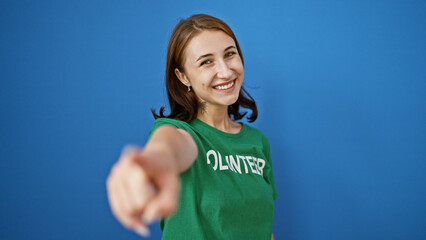 Young woman volunteer pointing to camera smiling over isolated blue background