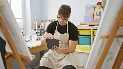 Attractive, serious young hispanic man artist, engrossed in sketching his portrait on canvas,...