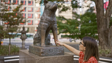 Alluring hispanic woman with glasses touches iconic hachiko statue on busy tokyo street â€“...