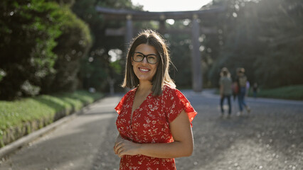 Cheerful, beautiful hispanic woman with glasses poses confidently, smiling at tokyo's meiji shrine,...