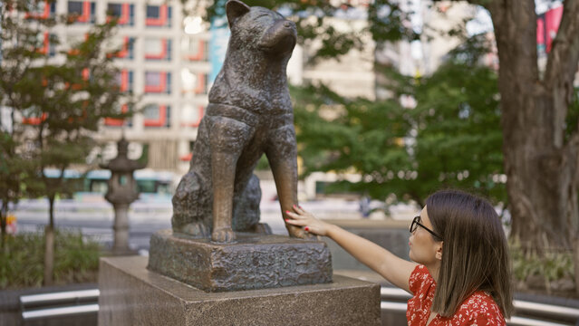 Alluring hispanic woman with glasses touches iconic hachiko statue on busy tokyo street â€“ immersed in japanese culture and traditions