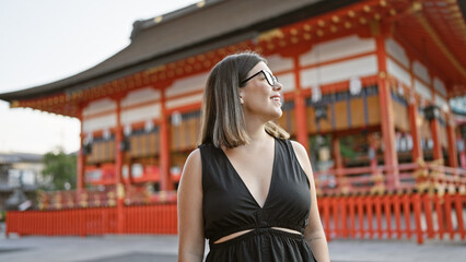 Confidently posing at fushimi inari taisha, a beautiful hispanic woman wearing glasses, smiles...
