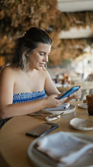 Young hispanic woman using smartphone sitting on the table at the restaurant