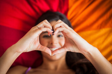 Teenage girl laying on bed making heart shape with hands