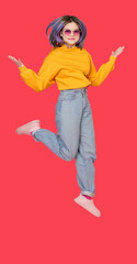 Smiling Asian girl teenager in mid-jump against vibrant red color background. Exuberance and...