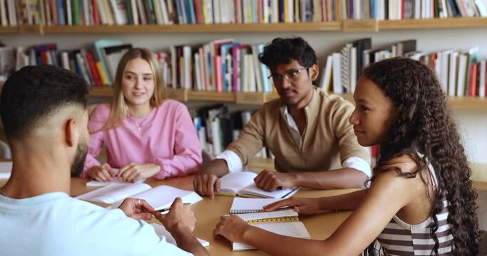 Group of multiracial teens students sit at desk in library talking about joint task, share ideas working on project take part in educational seminar studying together. Teamwork, education, knowledge
