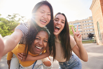 Three young multiracial friends taking selfie portrait together outdoors in summer. Latin woman...