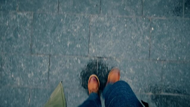 POV shot of a man's leather boots walking on wet urban pavement