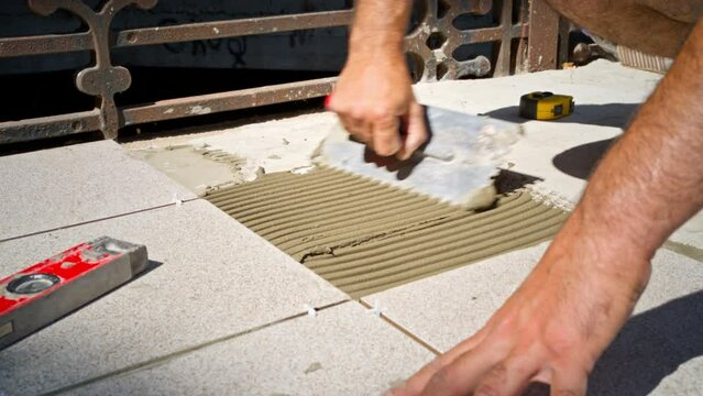 The tile stacker manually applies cement glue to the concrete to lay the floor tiles.