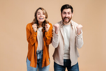 Excited, attractive couple, smiling man and woman wearing colorful clothes gesturing, victory