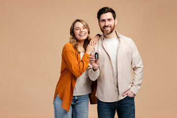 Portrait of happy couple, smiling man and woman wearing stylish colorful clothes, holding car key, looking at camera isolated on beige background. Buying car concept