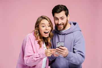 Attractive, excited couple wearing stylish colorful clothes, holding mobile phone, using mobile app