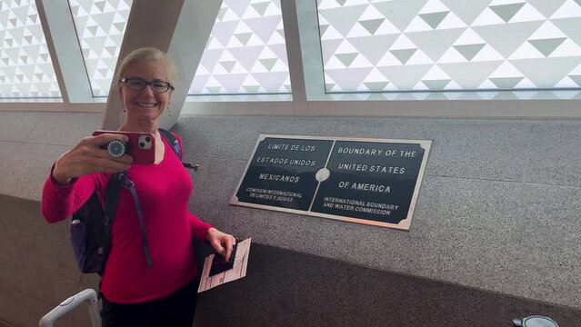 Woman taking a selfie of her in front of the Mexico USA border in the Cross Border Xpress bridge linking San Diego with Tijuana airport.