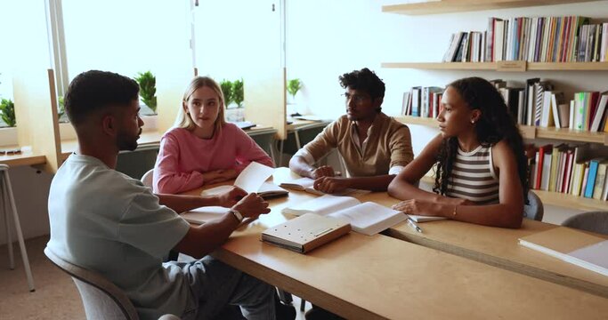 Multinational guys and girls sit at table in library, talking, thinking on solution, prepare essay, working on joint assignment, discuss higher institution admission, take part in educational seminar
