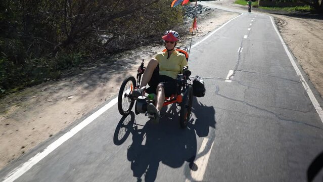 Elderly senior woman riding a recumbent electric bike on a bike path in Southern California. Filmed in slow motion.