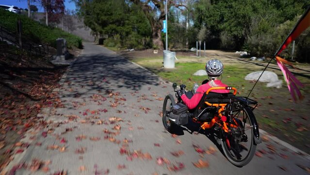 Elderly senior woman riding recumbent tricycle e-bike on a path on a sunny day in a park.