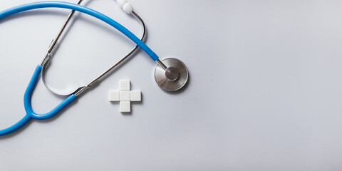 Blue stethoscope and white cross made of plastic cubes on gray background. Health insurance concept. Medical calendar. Selective focus, copy space