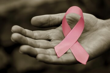 A photo of a pink cancer awareness ribbon in a hand. Illustration about breast cancer awareness. Hand holding pink ribbon on pink background.