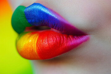 Close-up of lips artistically painted with the colors of the rainbow on a bright background.