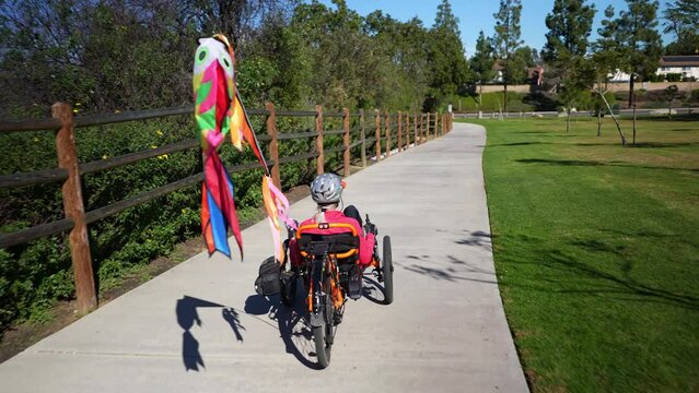 Elderly senior woman riding recumbent tricycle e-bike on a path on a sunny day in a park.