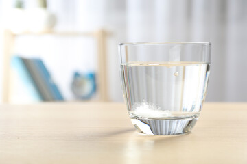 Glass of water with effervescent tablet on wooden table indoors, space for text