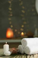 Fototapeta na wymiar Spa composition. Rolled towels, sea salt and burning candles on table against blurred lights, space for text