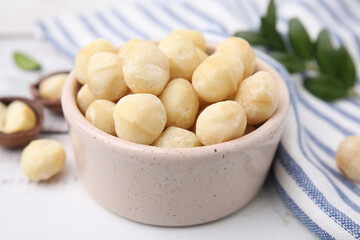 Tasty peeled Macadamia nuts in bowl on white table, closeup