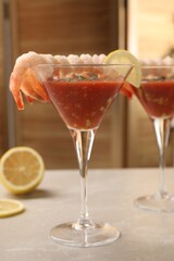 Tasty shrimp cocktail with sauce in glasses and lemon on light marble table