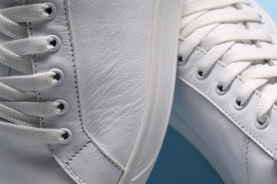 Pair of stylish white sneakers on light blue background, closeup