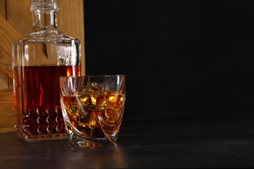 Whiskey in glass and bottle near wooden crate on dark table against black background. Space for text