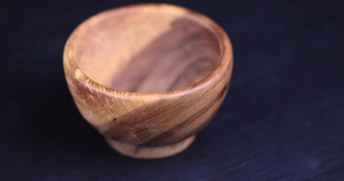an empty wooden bowl on a black slate table, a black background and a wooden food bowl