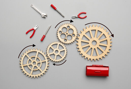 Flatlay picture of wooden gear, handy tool and toolbox on grey background. Mechanism repair.