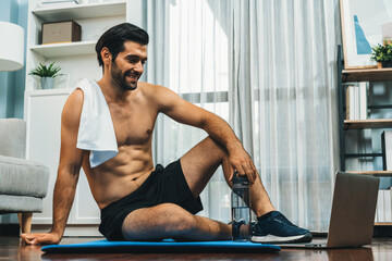 Athletic and sporty man resting on fitness mat during online body workout exercise session for fit...