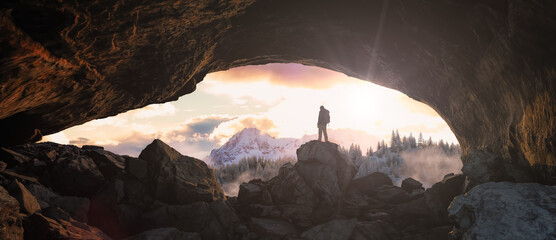 Adventure Man standing in rocky cave. Snow Covered Mountain Landscape in Background.