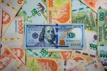 100 dollar note on a background of 1000 peso notes and 500 peso notes. USA and Argentina currencies. Monetary wallpaper.