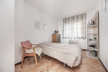 A bright bedroom in a house with white painted walls, a mirror on the wall, a chair for taking off shoes in the corner