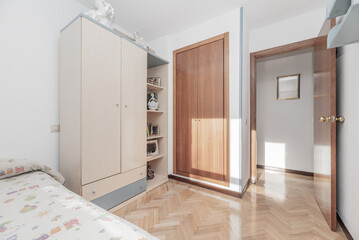A bright bedroom in a house with white painted walls, a mirror on the wall, regular and built-in wardrobes