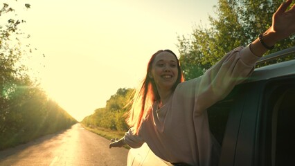 Smiling woman tourist enjoy freedom road trip in car window at sunset sunrise summer tree...