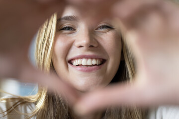 Close up portrait happy beautiful woman showing heart symbol with joined fingers staring at camera, having toothed smile advertising dental clinic professional services, check-up. Volunteering, love