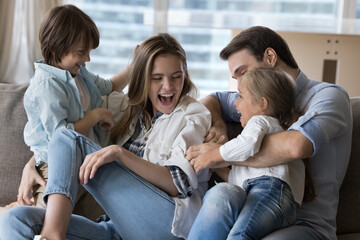 Cheery family with little kids play seated on couch. Loving cheerful parents, adorable son and...