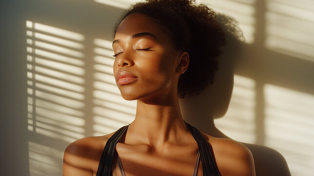 a beautiful woman posing by a window with her eyes closed facing the sun