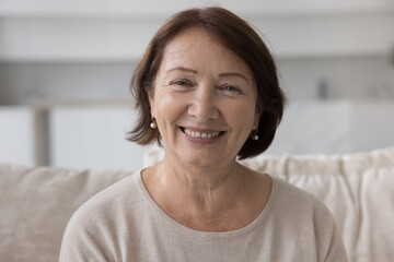 Positive mature older retired woman home head shot portrait. Female pensioner sitting on sofa,...